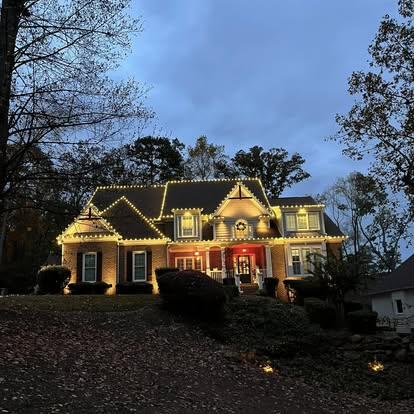 Brick home set on a rise, roofline lit at dusk with red accents at the entry and the sky still holding its blue
