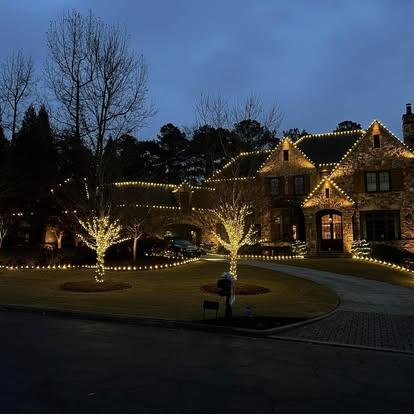 Brick estate at blue hour with two mature trees wrapped to full height beside a roundabout drive