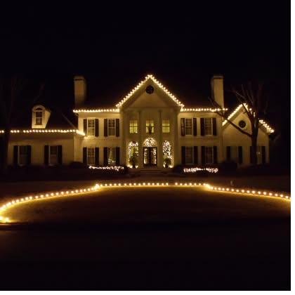 Cream Georgian home at night, roofline run in warm white with a centered entry wreath and the front bed edged in a single sweeping line