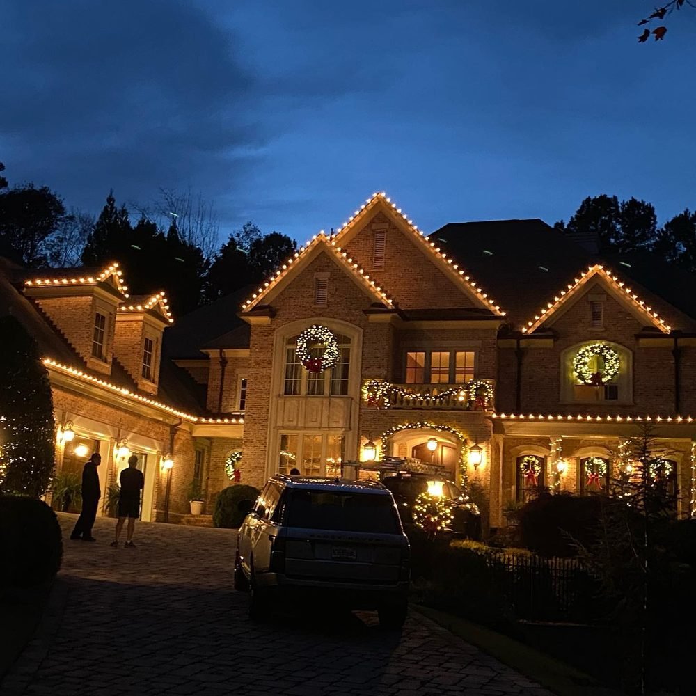 Brick estate photographed at blue hour, roofline picked out in warm white with a wreath on every gable