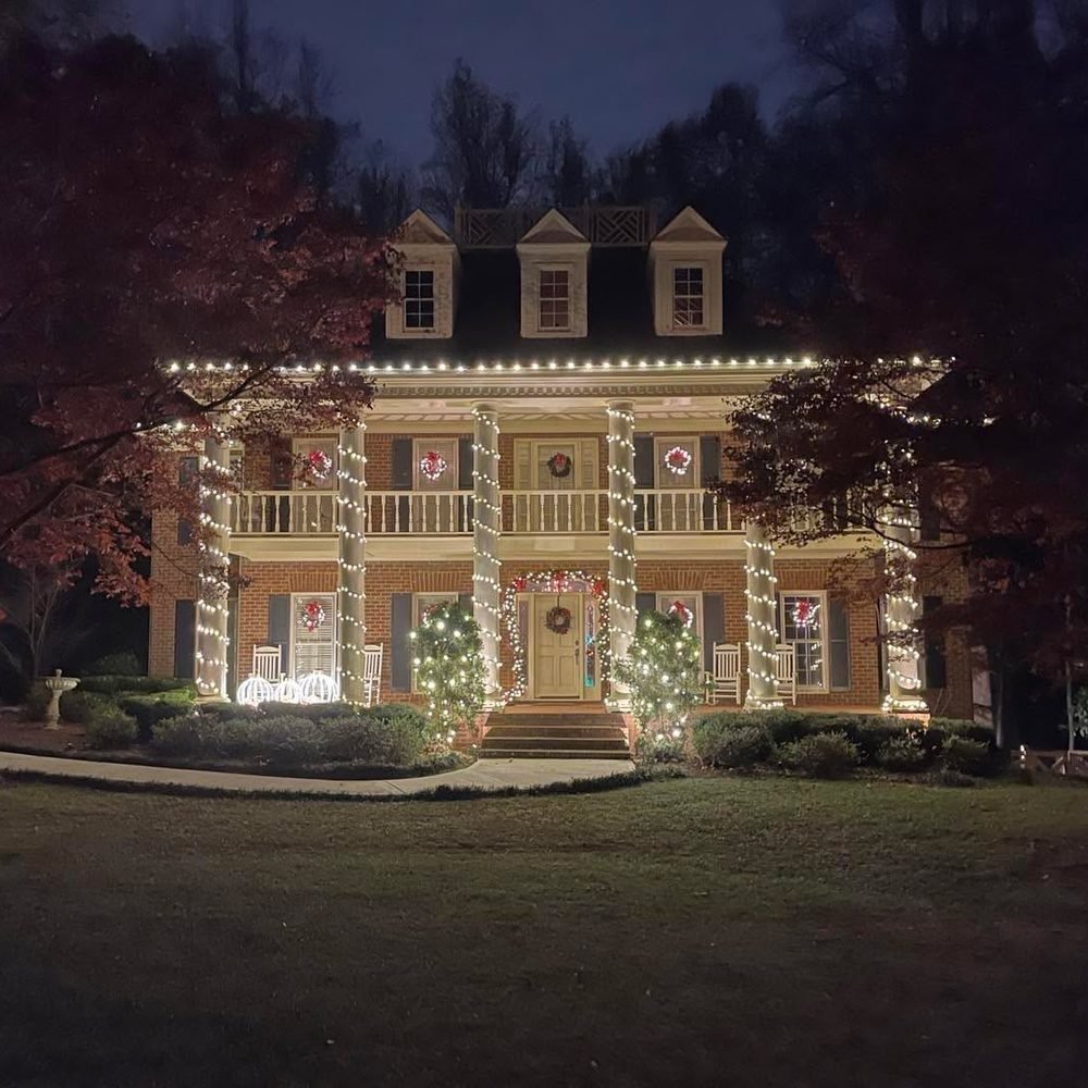 Brick colonial with garland-wrapped columns, a wreath in every window and lit trees flanking the door