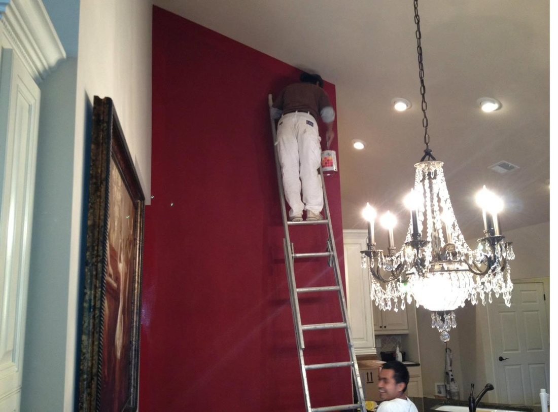 A Trademark Design painter on a ladder cutting in the top edge of a deep crimson feature wall in a kitchen