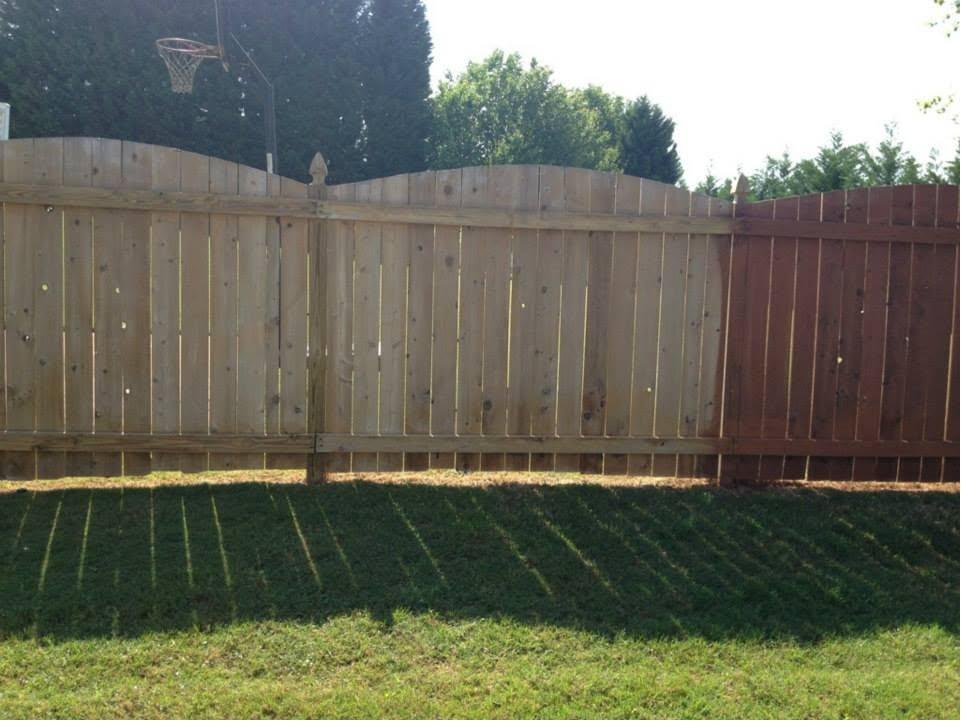 Privacy fence photographed mid-job, untreated grey timber on the left and freshly stained boards on the right