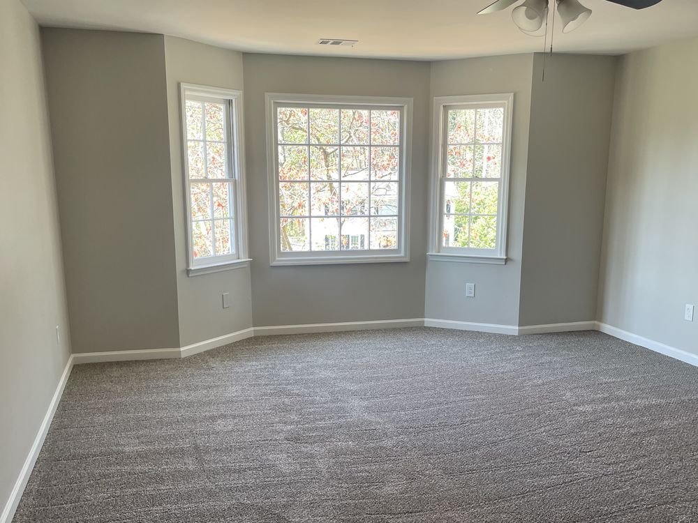 Empty living room painted in warm grey with white baseboards, casings and a three-panel bay window